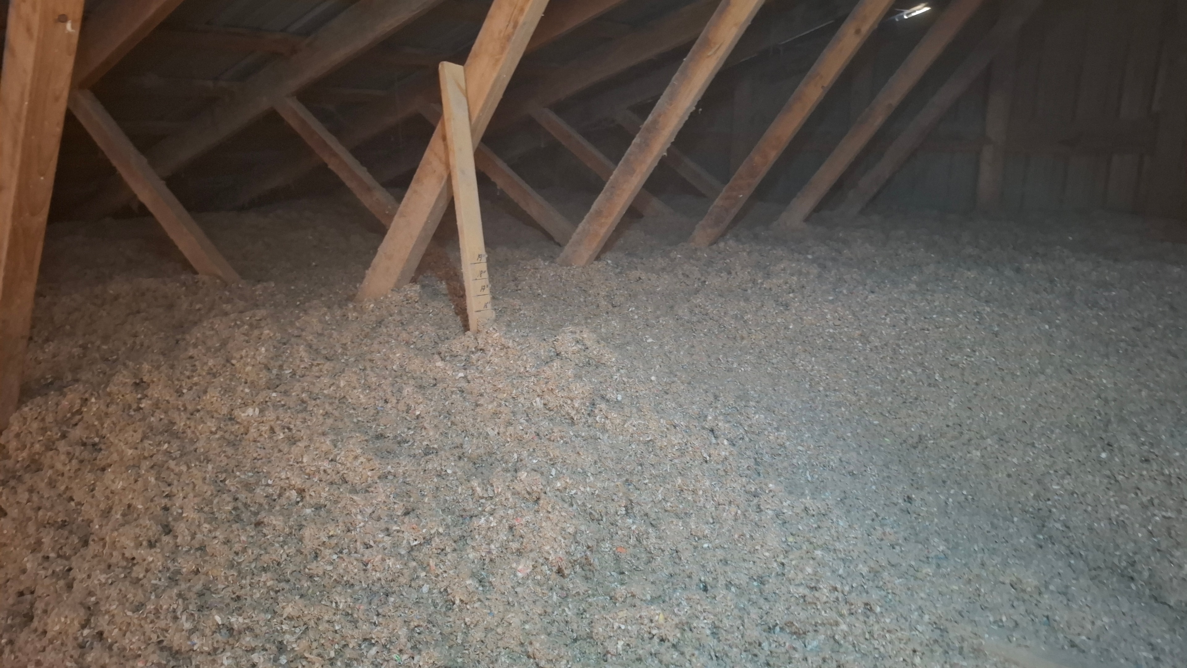 Blown-in cellulose insulation completed in new construction attic — depth gauge visible