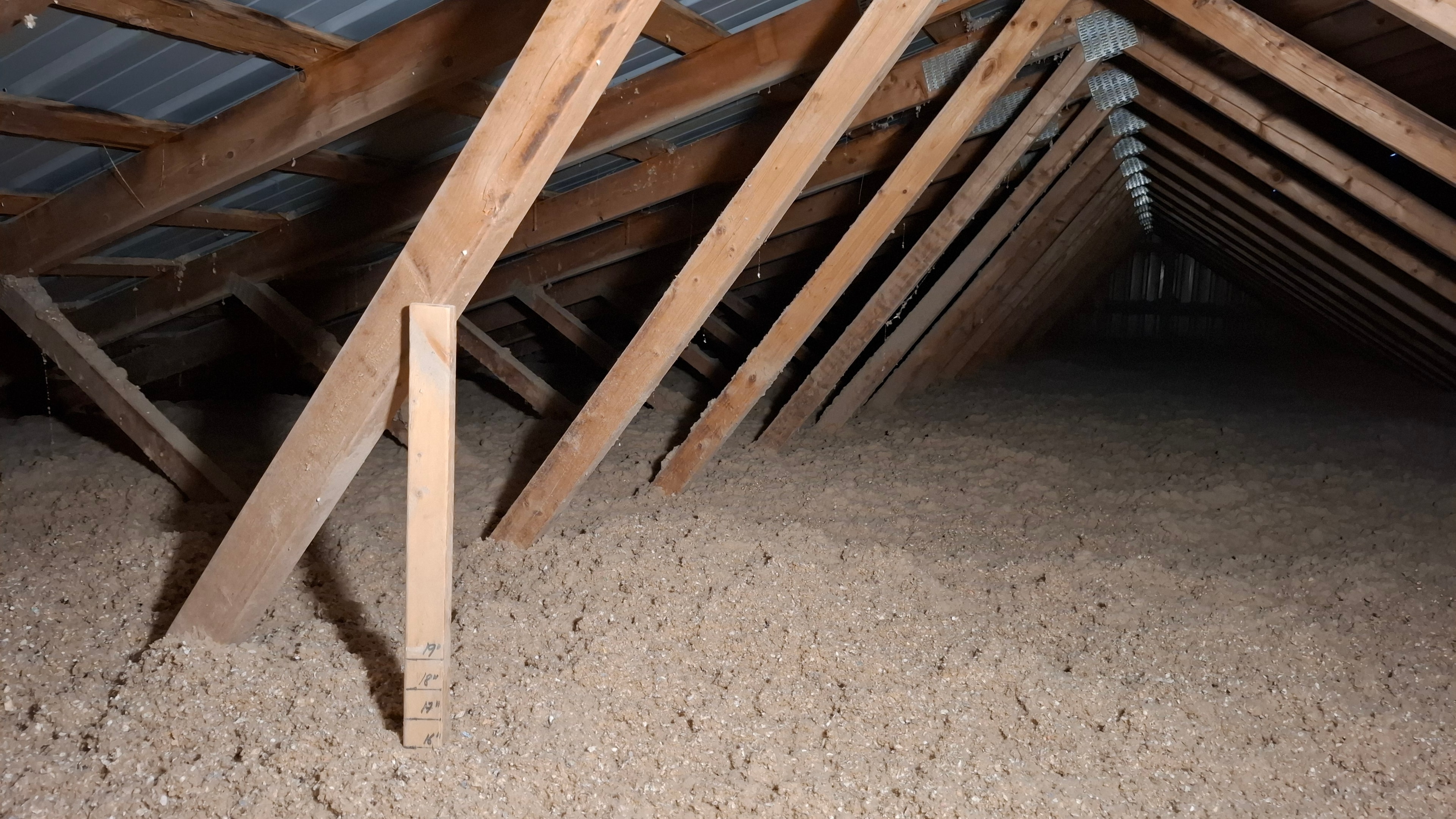 Completed attic cellulose insulation with depth gauge stick showing 19 inches