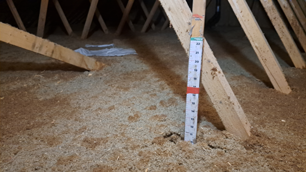 Attic before top-up showing existing insulation level with depth ruler — Ottawa residential