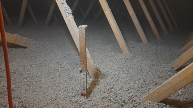 Completed blown-in attic insulation top-up with depth ruler confirming finished level — Ottawa residential