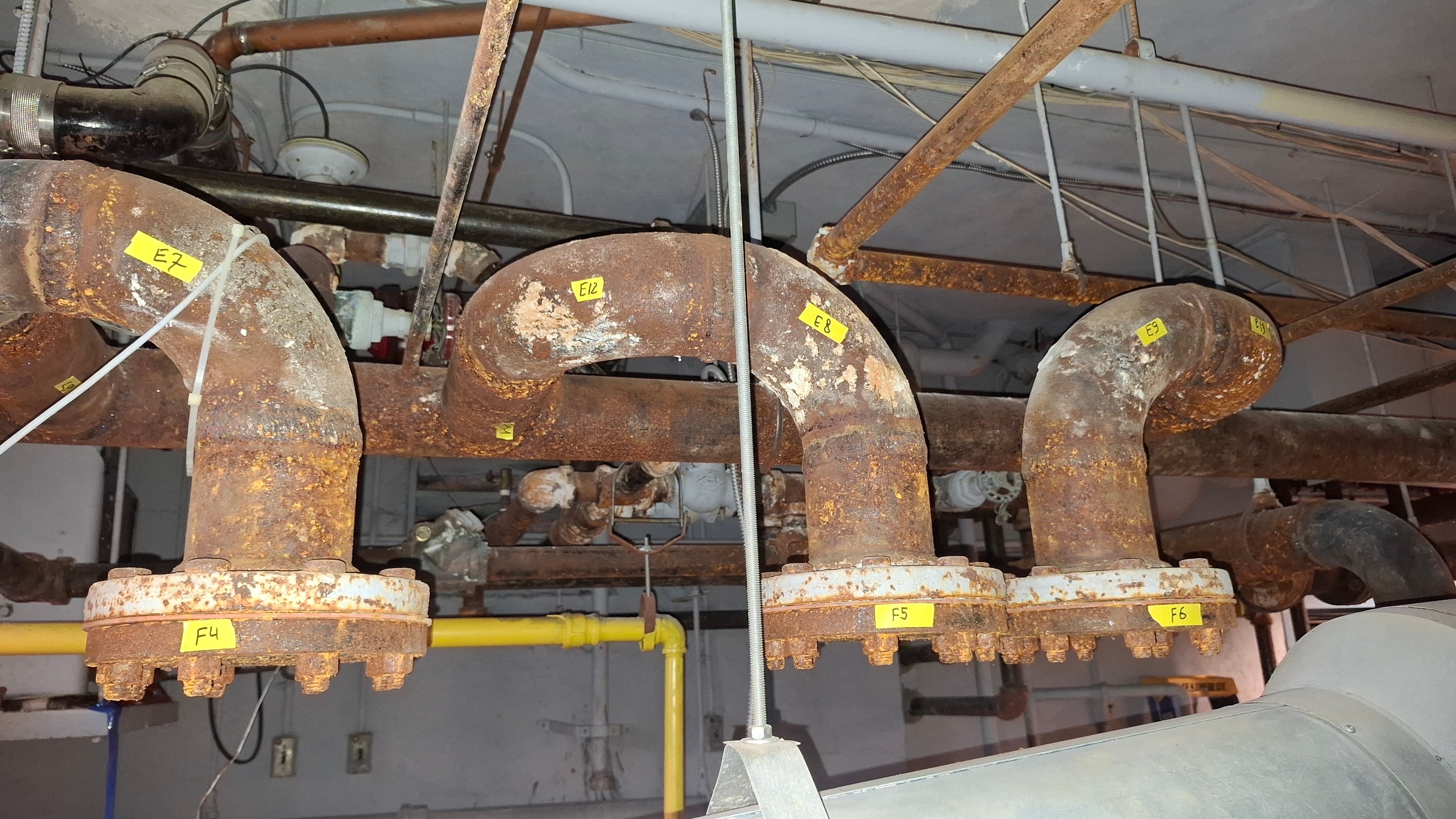 Before — heavily corroded bare pipe run beside mechanical equipment