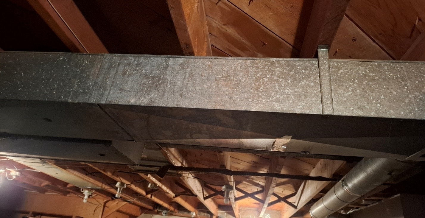 Close-up of main trunk duct with ACM asbestos paper still present — before removal