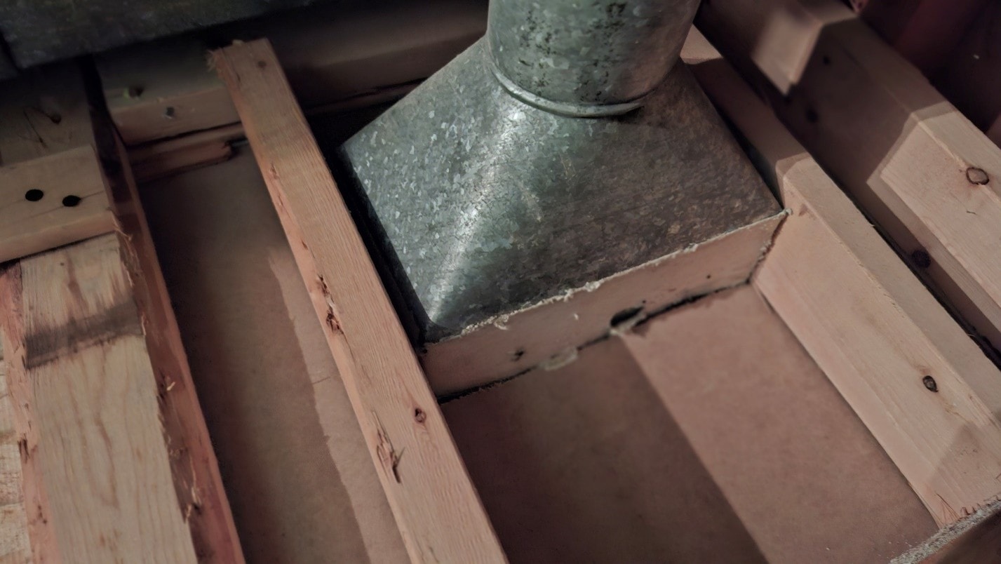 ACM paper on round duct boot penetrating floor framing — before removal