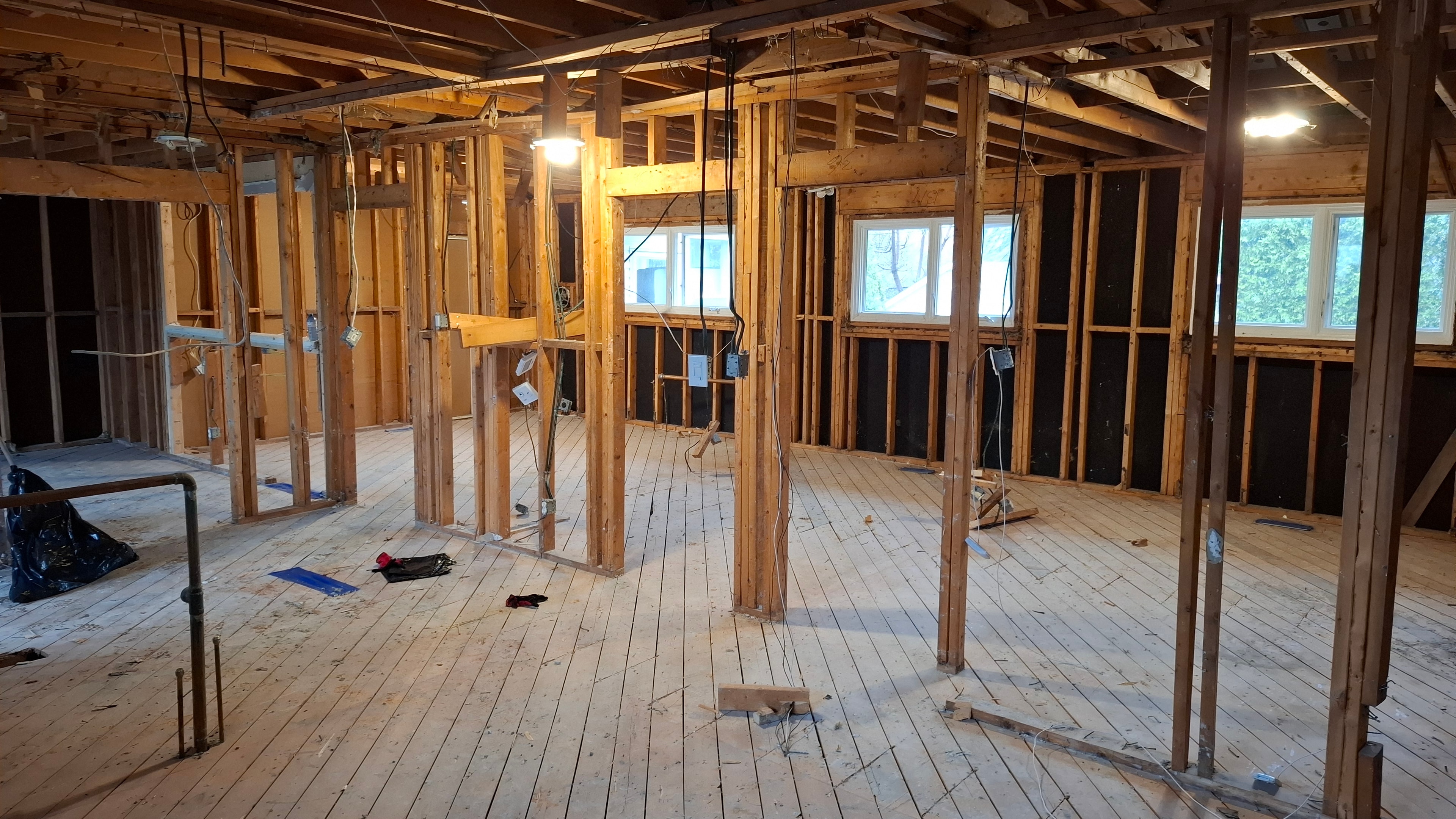 Fully gutted residential main floor — all walls stripped to framing, original hardwood subfloor exposed