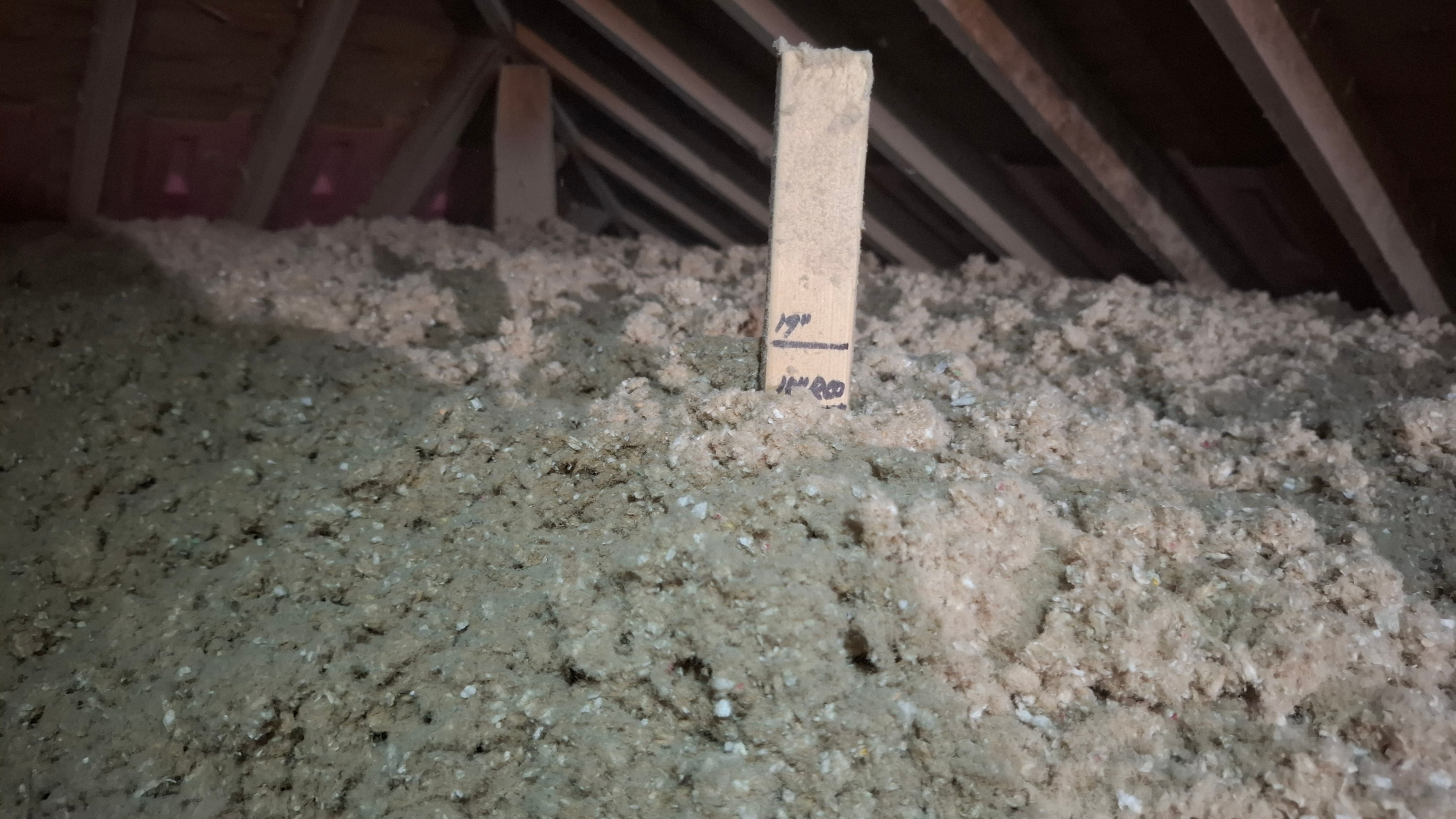 Depth ruler in blown-in cellulose attic insulation showing 19 inches depth — confirming approximately R60 thermal resistance