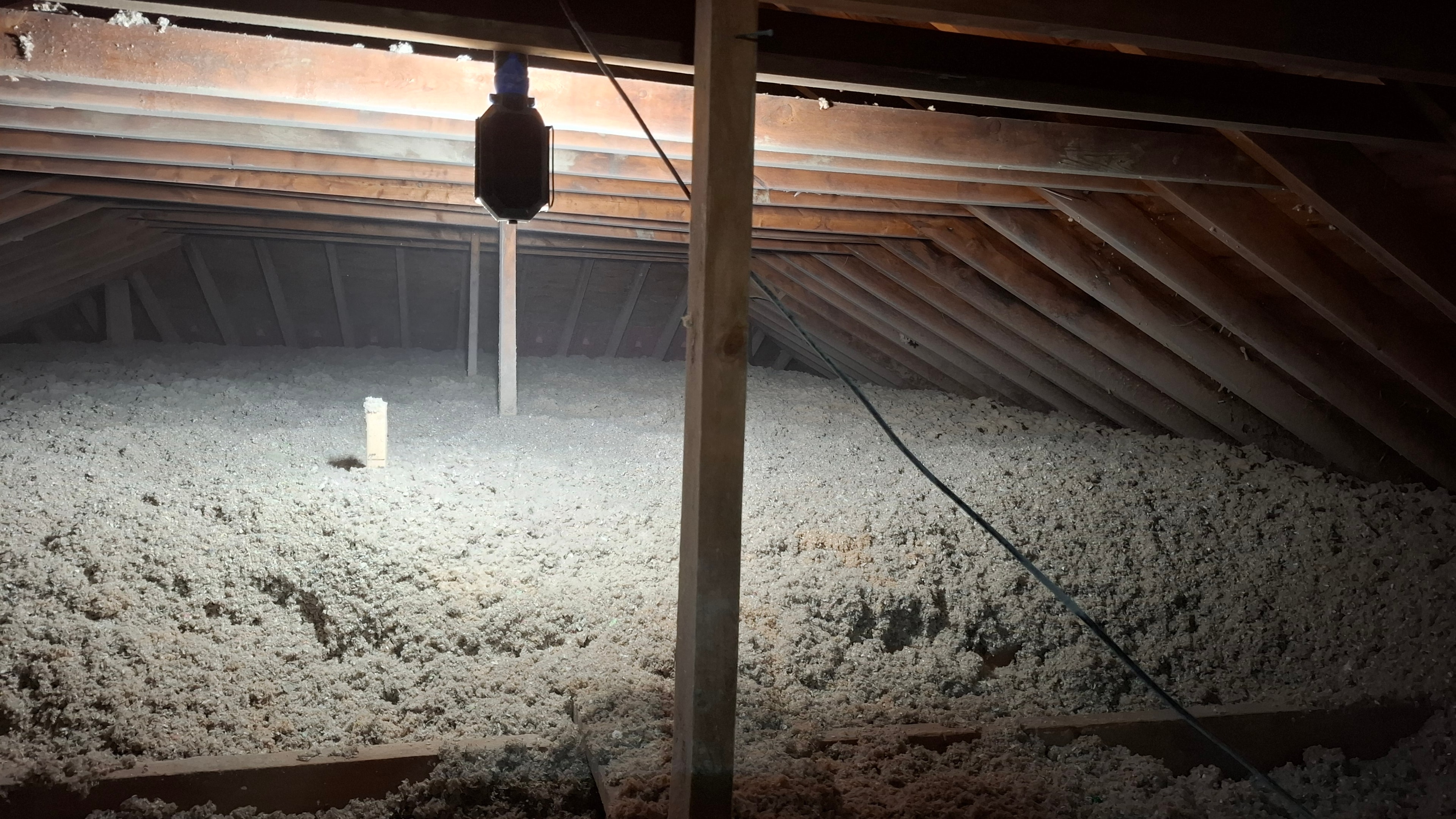 Wide attic view with work light showing completed blown-in cellulose insulation and depth ruler in foreground — Osgoode Ontario residential