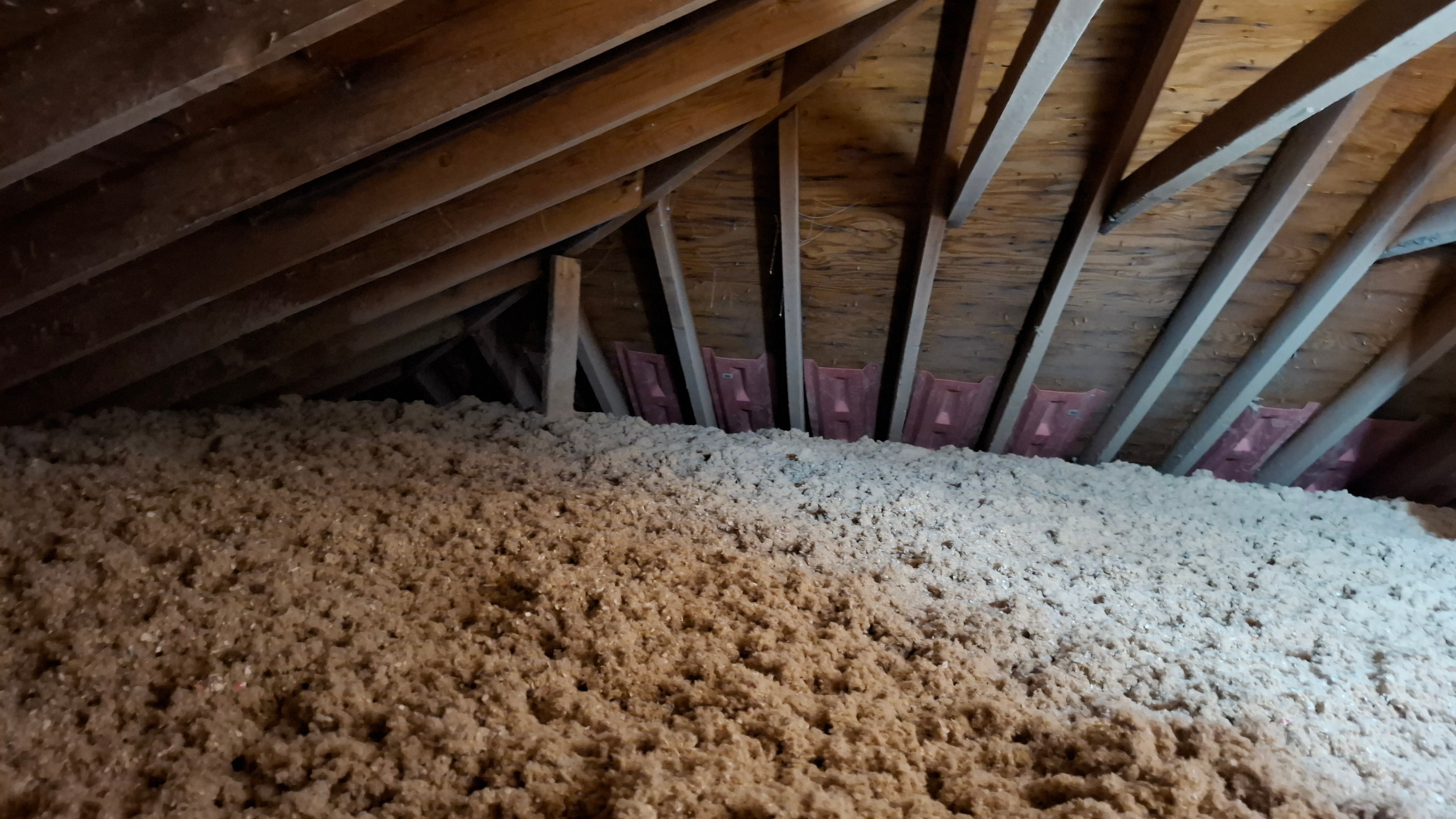Eave area showing blown-in cellulose insulation butting up against pink ventilation baffles — confirming baffles installed and insulation coverage extends to eaves