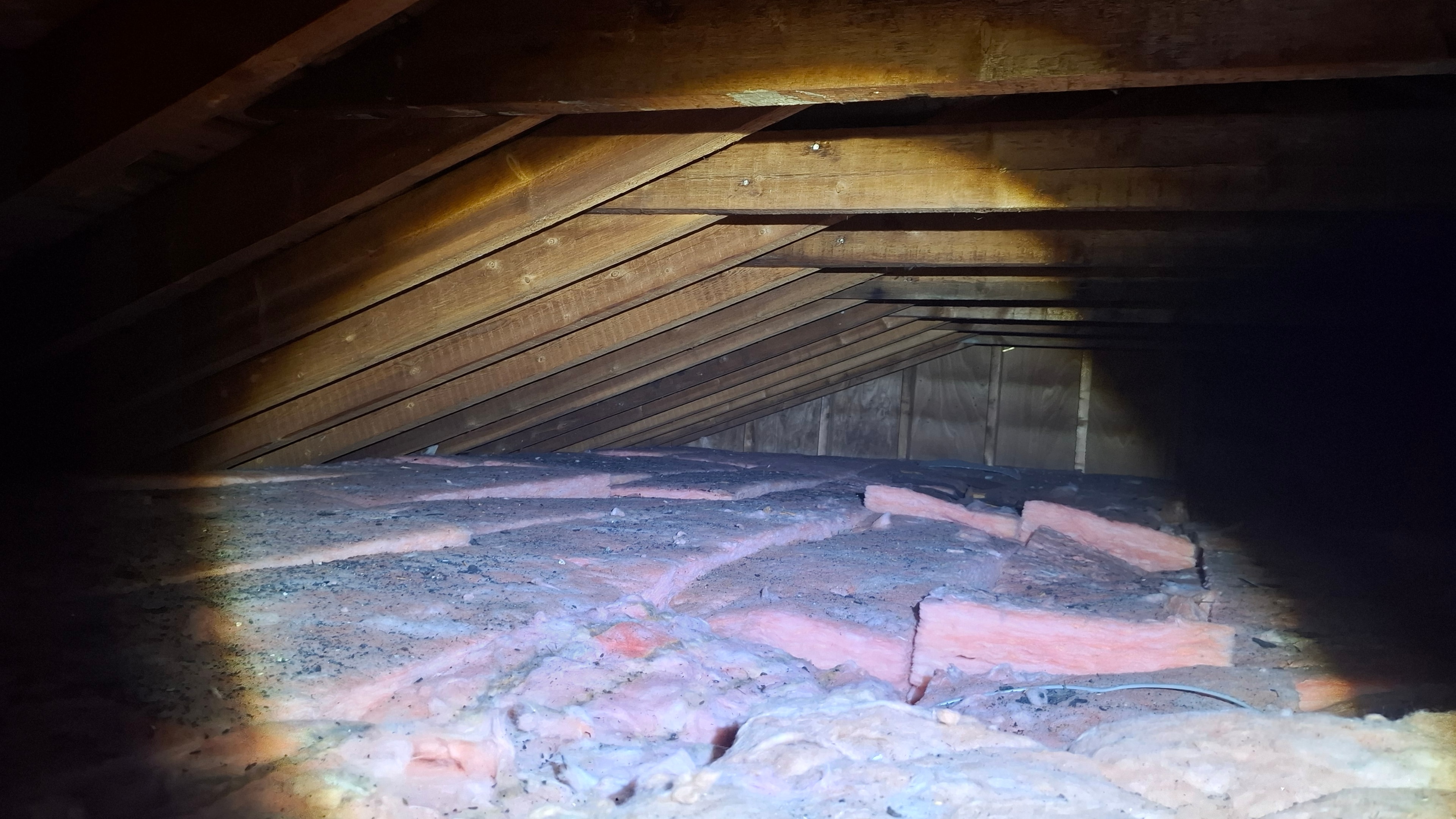 Attic space showing existing fiberglass batt insulation and vermiculite visible between joists
