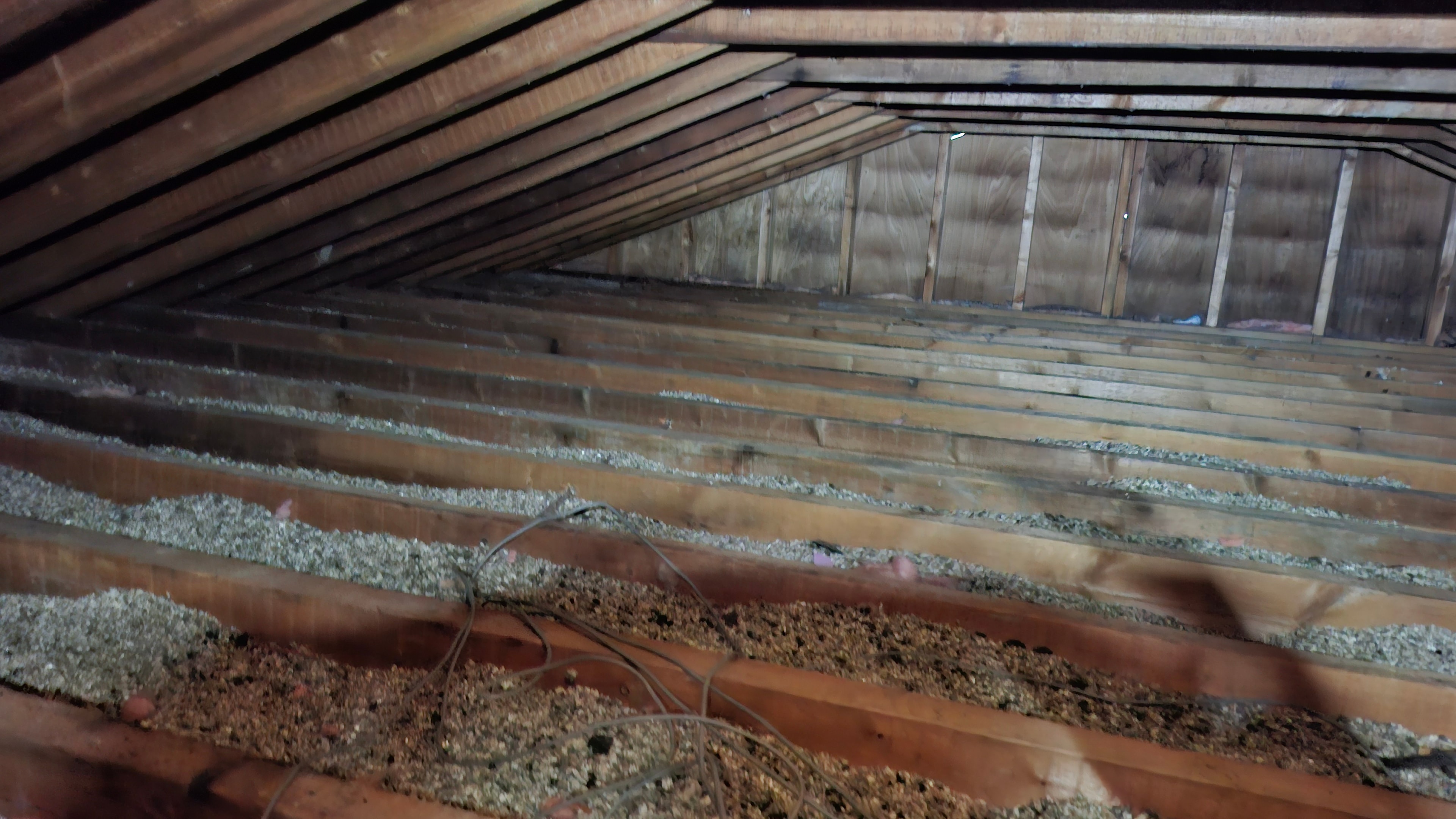 Wide view of attic showing extent of vermiculite coverage across floor joists